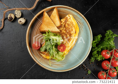 Omelet with cheese, salad and cherry tomatoes. A hot second course for breakfast of chicken eggs, cheese salad and vegetables. Classic vegetarian breakfast with toast. Omelet with cheese, salad and cherry tomatoes. A hot second course for breakfast of chicken eggs, cheese salad and vegetables. Classic vegetarian breakfast with toast. 73221411