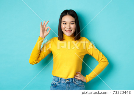 Happy beautiful asian woman smiling, showing okay gesture in approval, saying yes, standing pleased over blue background Happy beautiful asian woman smiling, showing okay gesture in approval, saying yes, standing pleased over blue background 73223448