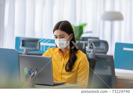 New normal of Asian woman in yellow shirt wearing surgical face mask working with computer laptop thinking to get ideas and requirement in Business startup at modern office or Co-working space New normal of Asian woman in yellow shirt wearing surgical face mask working with computer laptop thinking to get ideas and requirement in Business startup at modern office or Co-working space 73229740
