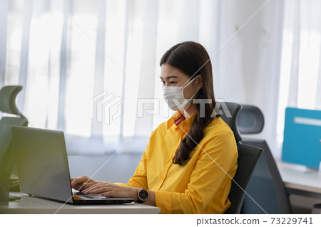 New normal of Asian woman in yellow shirt wearing surgical face mask working with computer laptop thinking to get ideas and requirement in Business startup at modern office or Co-working space New normal of Asian woman in yellow shirt wearing surgical face mask working with computer laptop thinking to get ideas and requirement in Business startup at modern office or Co-working space 73229741