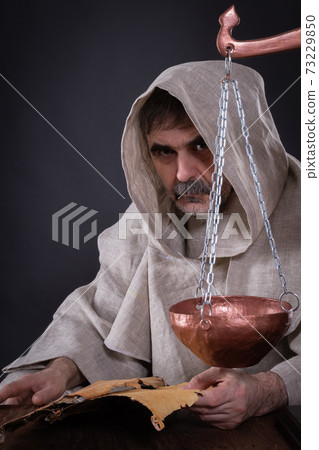 A monk alchemist is engaged in science, studying ancient manuscripts on birch bark 73229850