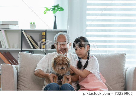 Asian Elderly and children sit on sofa and playing with dog together in living room at home 73229965