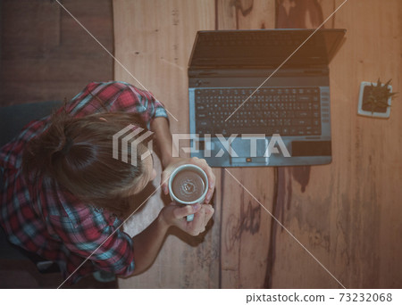 Beautiful woman drinking coffee or chocolate at cafe. Portrait of girl in a cafeteria drinking hot cappuccino and looking at cup..Woman holding a cup of coffee at the coffee shop from top view. 73232068