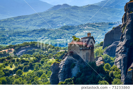 Close view of monastery of St Nicholaos Anapafsas on top of sedimentary pillar, green hills of Meteora valley at midday. Greece, UNESCO World Heritage 73233860