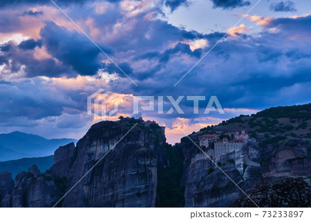Twilight over Varlaam and Great Meteoron monasteries in Meteora, Greece. Underexposed, great sunset with clouds and sun rays. UNESCO World Heritage Twilight over Varlaam and Great Meteoron monasteries in Meteora, Greece. Underexposed, great sunset with clouds and sun rays. UNESCO World Heritage 73233897