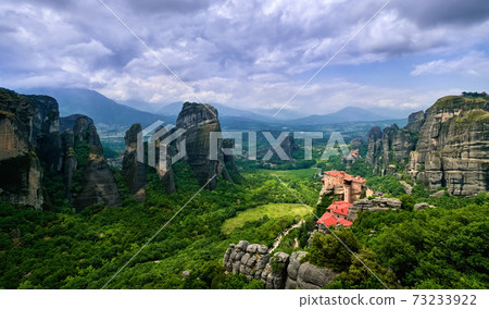 View over nunnery of Moni Agias Varvaras Roussanou, rocks of Meteora, Greece and valley. UNESCO World Heritage. Cloudy sky, sun rays fall on monastery 73233922