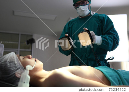 Team of professional surgeons performing operation in hospital , they are holding defibrillator and help while patient will die operation room at hospital 73234322