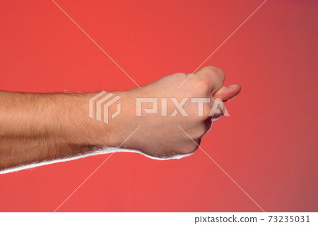 Man's hand with a fig's sign close-up is isolated on a red background Man's hand with a fig's sign close-up is isolated on a red background 73235031