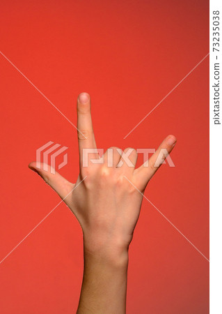 Human hand showing three fingers, symbolizing rock style, isolated on a red background 73235038