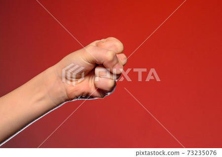 Human hand that squeezed fingers into a fist, symbolizing hatred and resistance, isolated on a red background Human hand that squeezed fingers into a fist, symbolizing hatred and resistance, isolated on a red background 73235076
