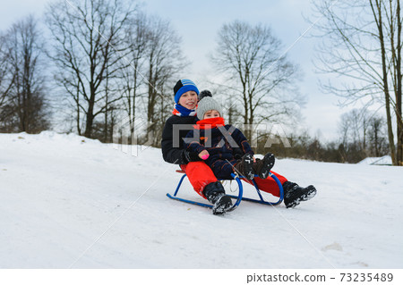 boy and girl are riding on sleds 73235489