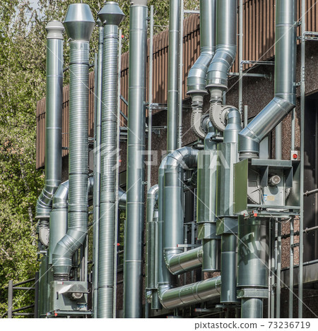 Abstract ensemble of shiny pipes on the wall of a building 73236719