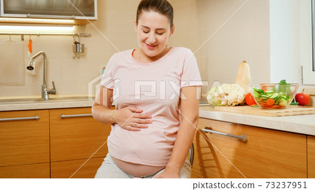 Portrait of smiling pregnant woman sitting on chair in kitchen after doing housework and cooking Portrait of smiling pregnant woman sitting on chair in kitchen after doing housework and cooking 73237951