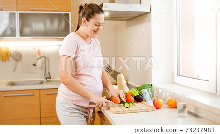 Happy smiling pregnant woman cutting vegetables and cooking on kitchen at home. Concept of healthy lifestyle and nutrition during pregnancy 73237981