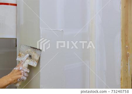 Builder puts plaster on the wall hand holding a spatula with construction repair the wall a putty finishing works 73240758