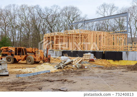 A woodentruss being lifted by a boom truck forklift in the building materials a stack of boards wood frame a new home A woodentruss being lifted by a boom truck forklift in the building materials a stack of boards wood frame a new home 73240813