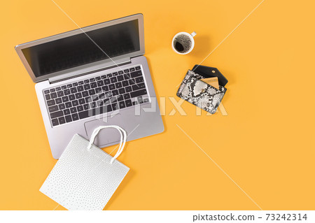 Laptop with shopping bags on trendy yellow orange background 73242314