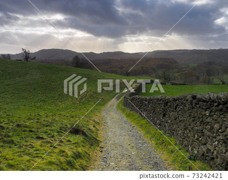 Path by dry-stone wall with rays of sunlight in a stormy sky, Lake District Path by dry-stone wall with rays of sunlight in a stormy sky, Lake District 73242421