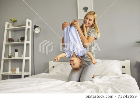 Happy mom playing with her toddler son holding him upside down sitting on bed in the morning 73242659