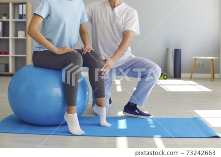 Woman doing exercise on fit ball with professional physiotherapist or chiropractor helping her Woman doing exercise on fit ball with professional physiotherapist or chiropractor helping her 73242663