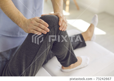 Hands of professional doctor osteopath checking patients knee during visit Hands of professional doctor osteopath checking patients knee during visit 73242667