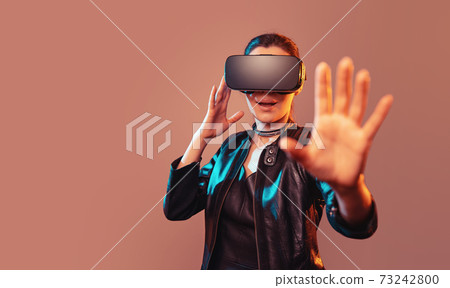 Young girl getting experience VR headset is using augmented reality eyeglasses being in virtual reality. Girl with hands up wearing virtual reality goggles. Woman touching air during VR experience Young girl getting experience VR headset is using augmented reality eyeglasses being in virtual reality. Girl with hands up wearing virtual reality goggles. Woman touching air during VR experience 73242800