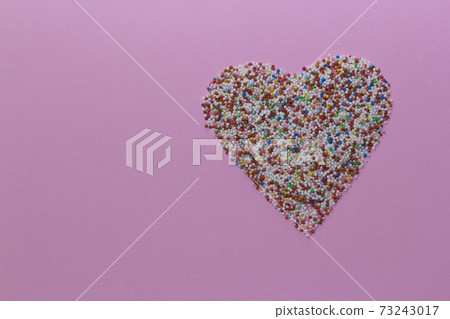 Sprinkles arranged in a heart shape on a pink rustic background. Valentine's Day, greeting card. Sprinklers for confectionery and pastry. Copy space,top view 73243017