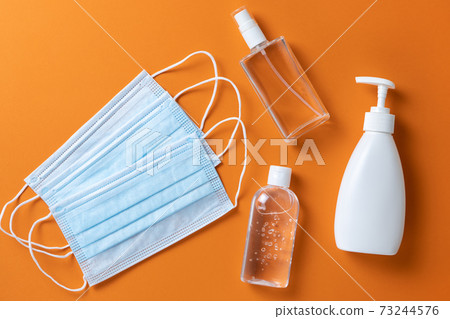 Medical protective, face masks, sanitizer gel, spray, liquid hand soap on orange background, close-up, flatly, minimal. Hygiene concept, protective equipment, prevention of spread of viral infections 73244576