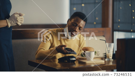 Black man paying with smartphone for order in cafe 73246531