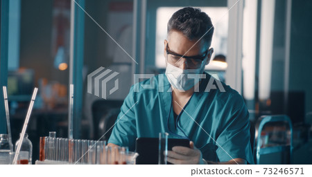 Male doctor analyzing samples and using tablet in lab 73246571