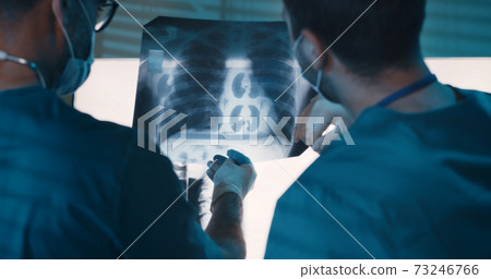 Male doctors examining X ray against lamps Male doctors examining X ray against lamps 73246766