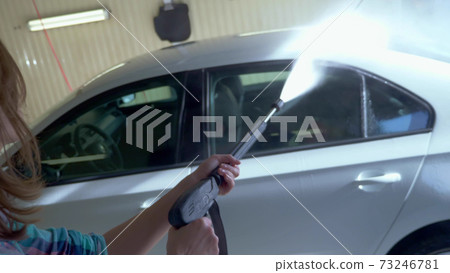 young woman washes a car at a self-service car wash. overall plan young woman washes a car at a self-service car wash. overall plan 73246781
