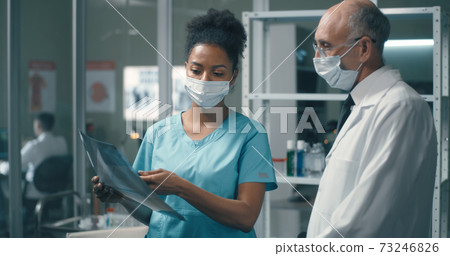 Black doctor discussing X ray with mature colleague Black doctor discussing X ray with mature colleague 73246826