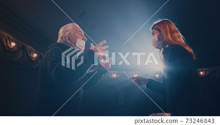 Actors in masks quarreling on stage in spotlight 73246843