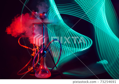 two smoky hookahs with glass flasks of water with shisha coals with red green neon lighting two smoky hookahs with glass flasks of water with shisha coals with red green neon lighting 73254691