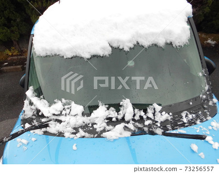 Snow piled up on the windshield of a car. The morning after a heavy snowfall. A snow-covered blue car. Winter scenery. 73256557