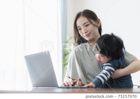 一位年輕的母親抱著一個0歲的嬰兒在操作電腦 73257070