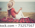 Fashion young lady viewed from back relax and enjoy the ocean view sitting on the field grass with cup of coffee - concept of tourist and spring summer holidays vacation outdoor activity 73257567