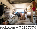 Couple lay down on the bed inside a vintage van - summer alternative holiday vacation with young people in love parked in front of a sunny beach and blue free horizon sky 73257570