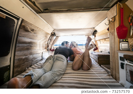 Couple lay down on the bed inside a vintage van - summer alternative holiday vacation with young people in love parked in front of a sunny beach and blue free horizon sky Couple lay down on the bed inside a vintage van - summer alternative holiday vacation with young people in love parked in front of a sunny beach and blue free horizon sky 73257570