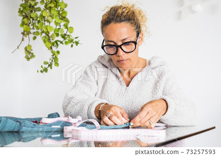 Adult woman concentrated in home work activity like tailor - clothing job with single female people working indoor in diy hand made clothes making of Adult woman concentrated in home work activity like tailor - clothing job with single female people working indoor in diy hand made clothes making of 73257593