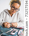 Portrait of middle age caucasian woman working at home tailoring with clothes to repair or hand made - tailor job with independent people in home work leisure activity 73257594