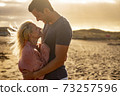 People in love and golden sunset outdoor - man and woman couple hug and look each other with beach in background - concept of protection and life together forever 73257596
