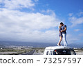 Love and travel people lifestyle - standing couple on the roof vehicle van together kissing and hugging with long road and blue sky in background for destination concept.- free lifestyle and 73257597