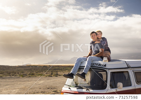 Young love couple sit down on a roof van enjoy travel lifestyle and holiday vacation together - concept of van life and free alternative trip with pretty couple enjoying outdoor and hug Young love couple sit down on a roof van enjoy travel lifestyle and holiday vacation together - concept of van life and free alternative trip with pretty couple enjoying outdoor and hug 73257598