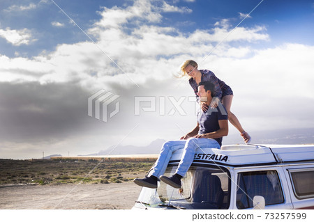 Happy couple enjoy the roof van together having fun in travel holiday alternative vacation - people together in road trip with transport vehicle and love life concept with blue sjy in background and 73257599