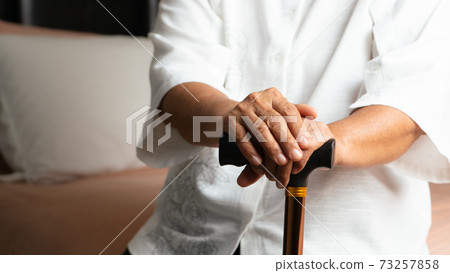 Senior back pain woman with walking stick at home 73257858