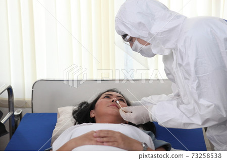 Doctors in full protective gear collects a sample from a mature woman on bed as part of the operations of a coronavirus mobile testing unit. Doctors in full protective gear collects a sample from a mature woman on bed as part of the operations of a coronavirus mobile testing unit. 73258538