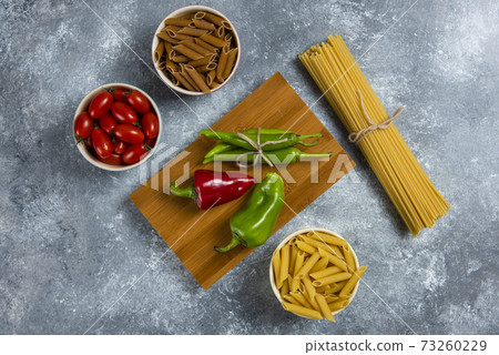 Raw spaghetti with vegetables on a wooden board Raw spaghetti with vegetables on a wooden board 73260229