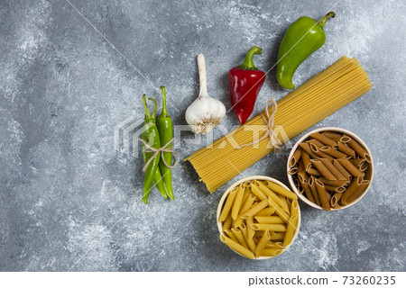 Raw spaghetti with vegetables on a wooden board Raw spaghetti with vegetables on a wooden board 73260235
